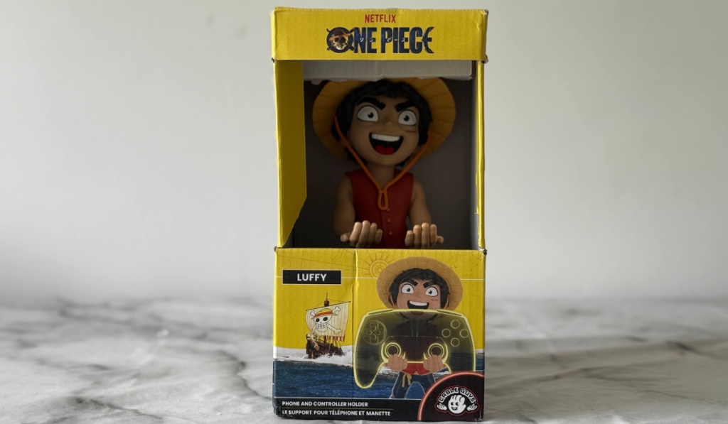 A boxed cable guys figure of Luffy from One Piece, designed as a phone and controller holder, set against a blurred marble background.