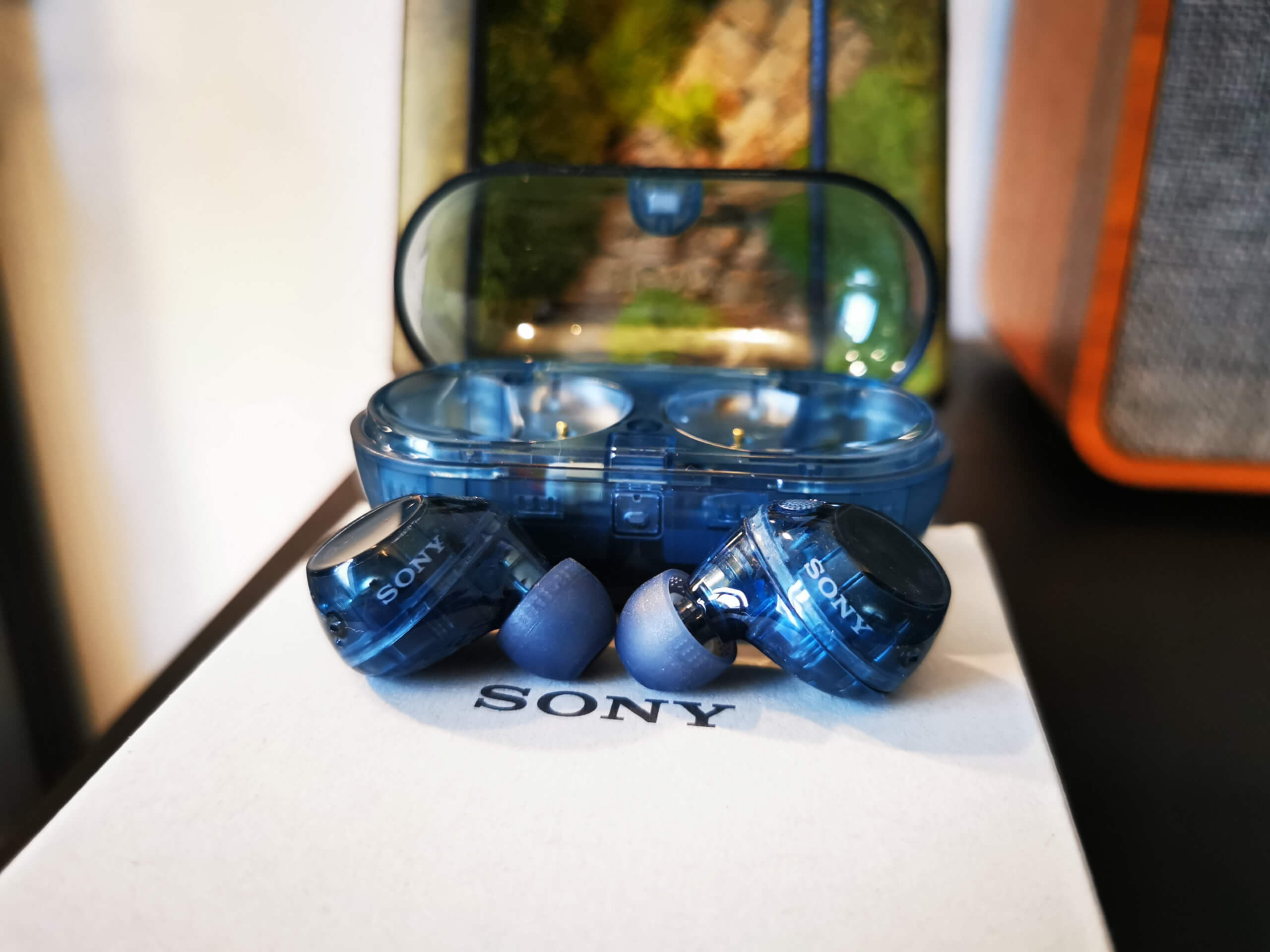 The Sony WF-C710N earbuds in transparent blue pictured in front of their open case on top of the white Sony box