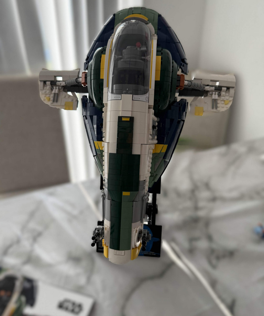 A detailed LEGO model of the Jango Fett's Firespray-Class Starship featuring a glass cockpit, dual side engines, and intricate designs atop a marble surface.