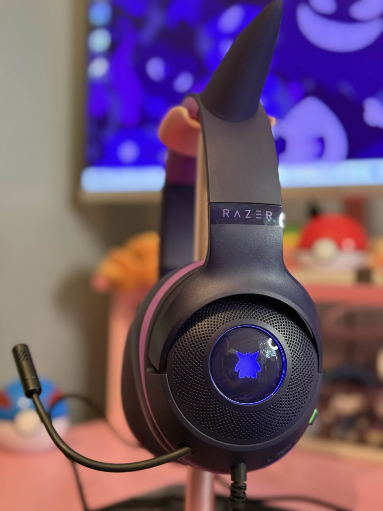 Close-up of a Razer gengar headset with a blue illuminated logo, mic attached, against a colourful ghost pokemon computer background.