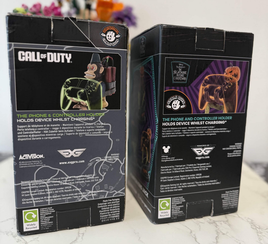 Two back boxes of gaming accessories: a phone/controller holder featuring Call of Duty and Nightmare Before Christmas designs, on a marble surface.