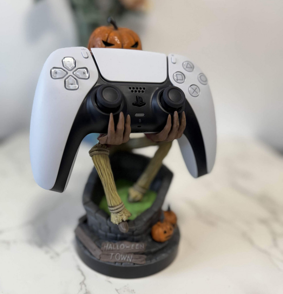 A pumpkin king jack from nightmare christmas cable guys controller holder holds a PS5 controller,. The figure features pumpkins and a playful design.