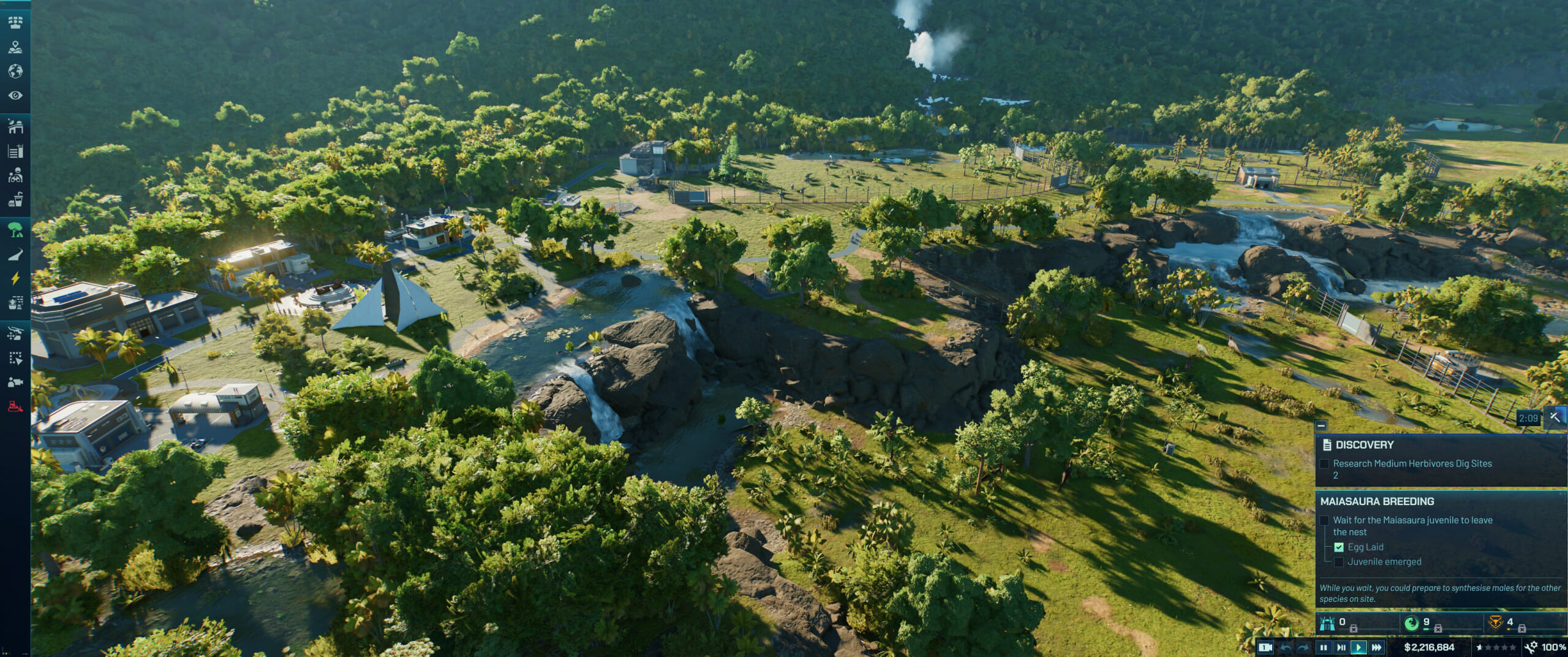 A lush, tropical landscape featuring a dinosaur park with buildings, waterfalls, and a breeding facility for Maiasaura.