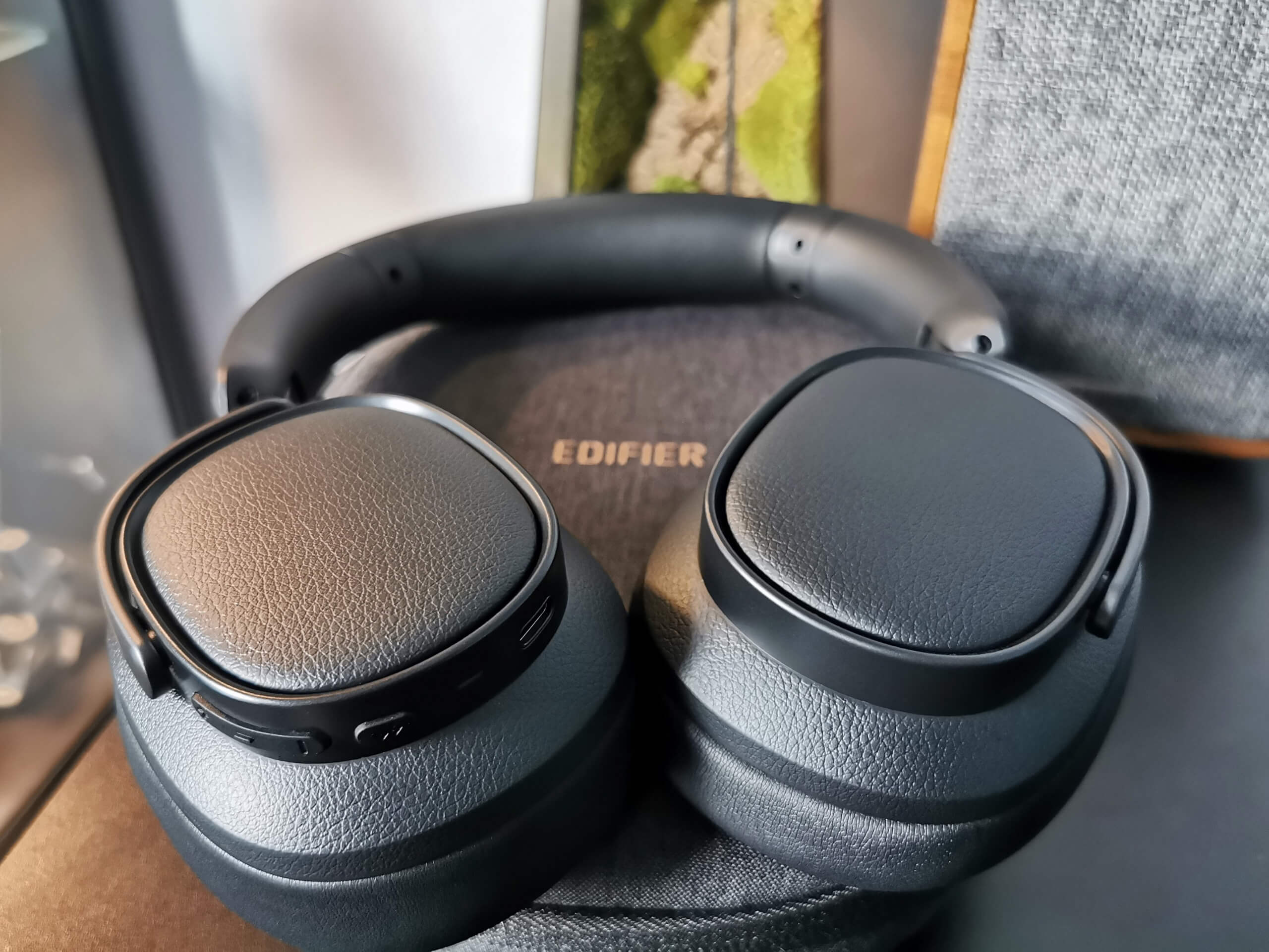 Edifier ES850NB pictured with the earcups folded flat on top of their grey travel case, showing the buttons and ports on the bottom of the right earcup. All on a black desk