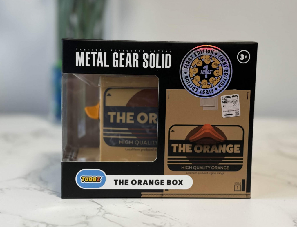 A collectible rubber duck TUBBZ figure featuring "The Orange Box" from Metal Gear Solid, with a clear display and first edition sticker.