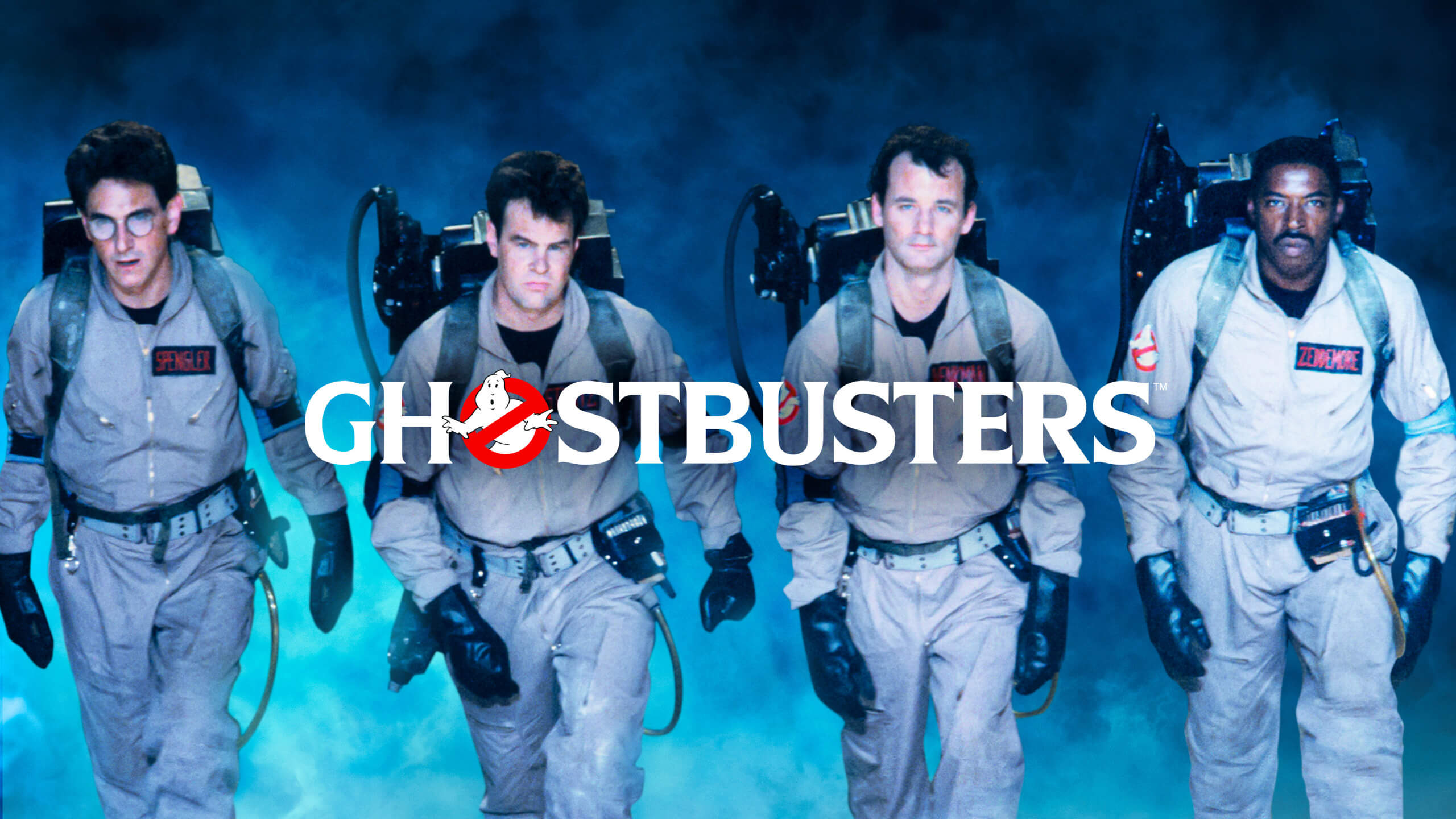 Four men in tan jumpsuits and proton packs stride forward through blue fog, with a large "Ghostbusters" logo over them, conveying determination.