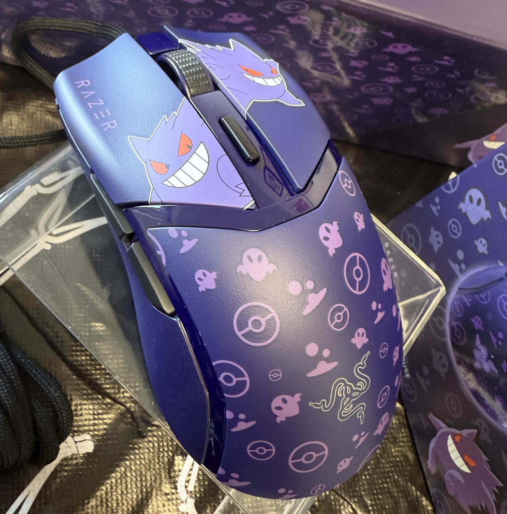 A purple Razer cobra gaming mouse featuring playful Gengar designs and Poké Balls, displayed on a clear stand against a dark background.