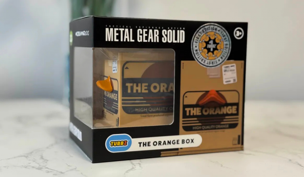 A collectible box labelled "The Orange Box" from Metal Gear Solid, featuring an orange-shaped figure inside a clear display case.