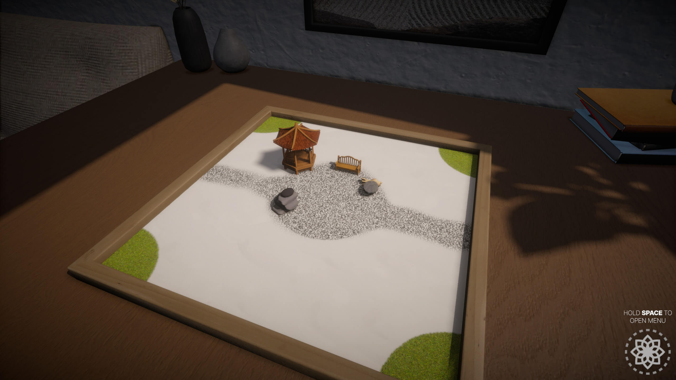 A miniature zen garden on a wooden table, featuring a gazebo, bench, stones, and decorative sand patterns.