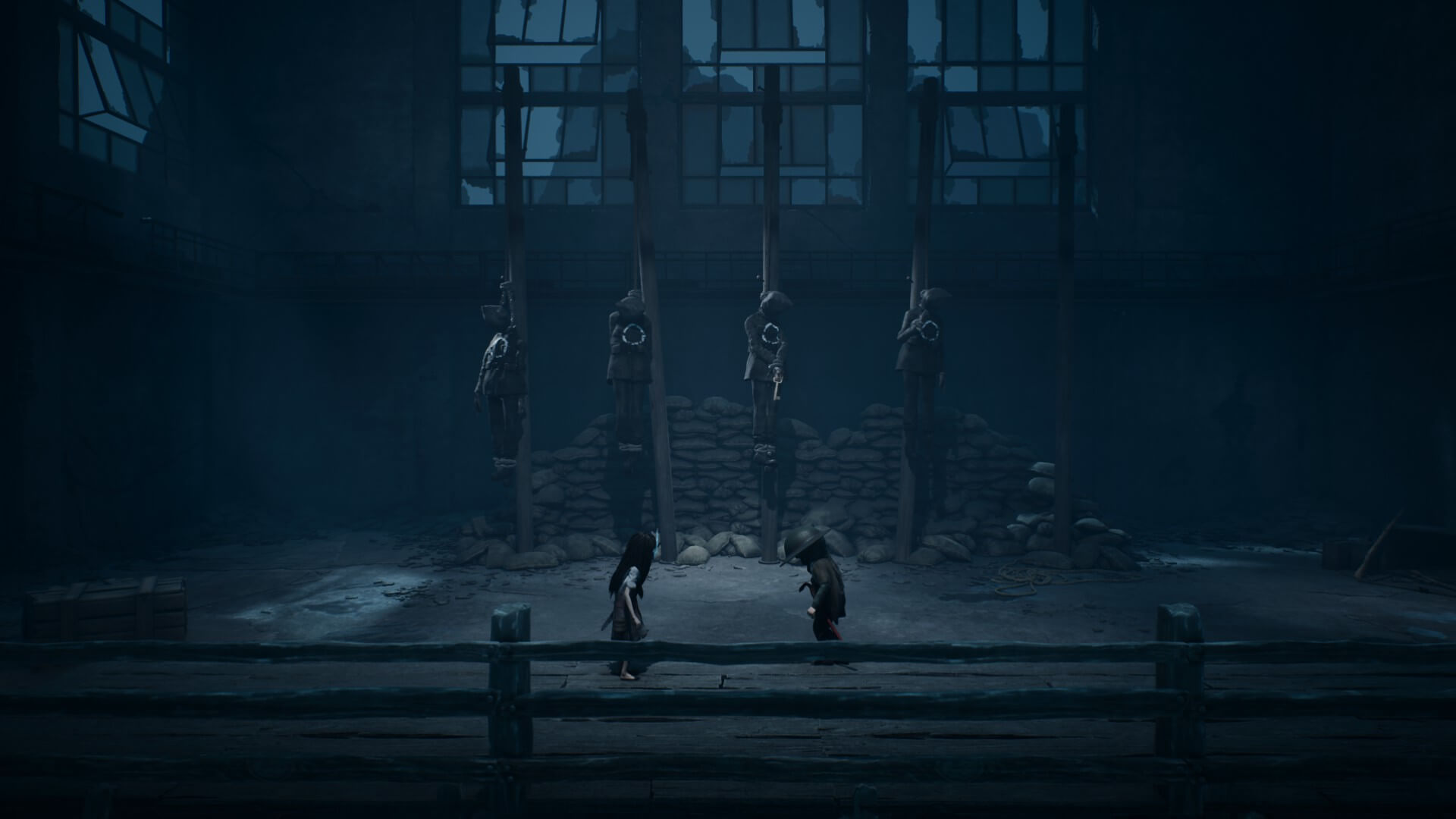 A dark scene of four bodies hanging, each has a target on them, but one has a bronze key as well. All the heads are covered with a burlap sack. Two children are closer to the screen looking at the bodies, one is wearing a helmet that looks like it is from World War 1. 