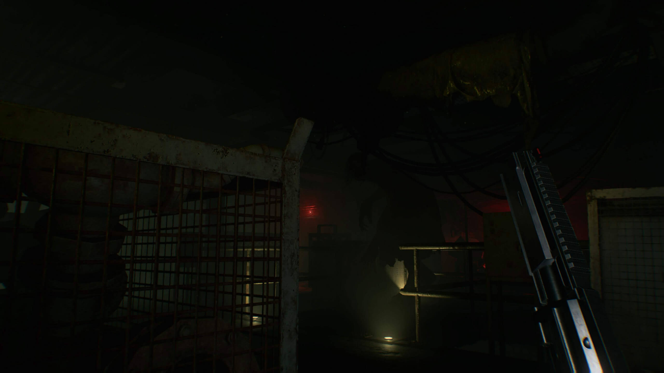 Dimly lit industrial room with metal fencing, exposed pipes, and red warning lights; a shotgun is visible in the lower right corner.