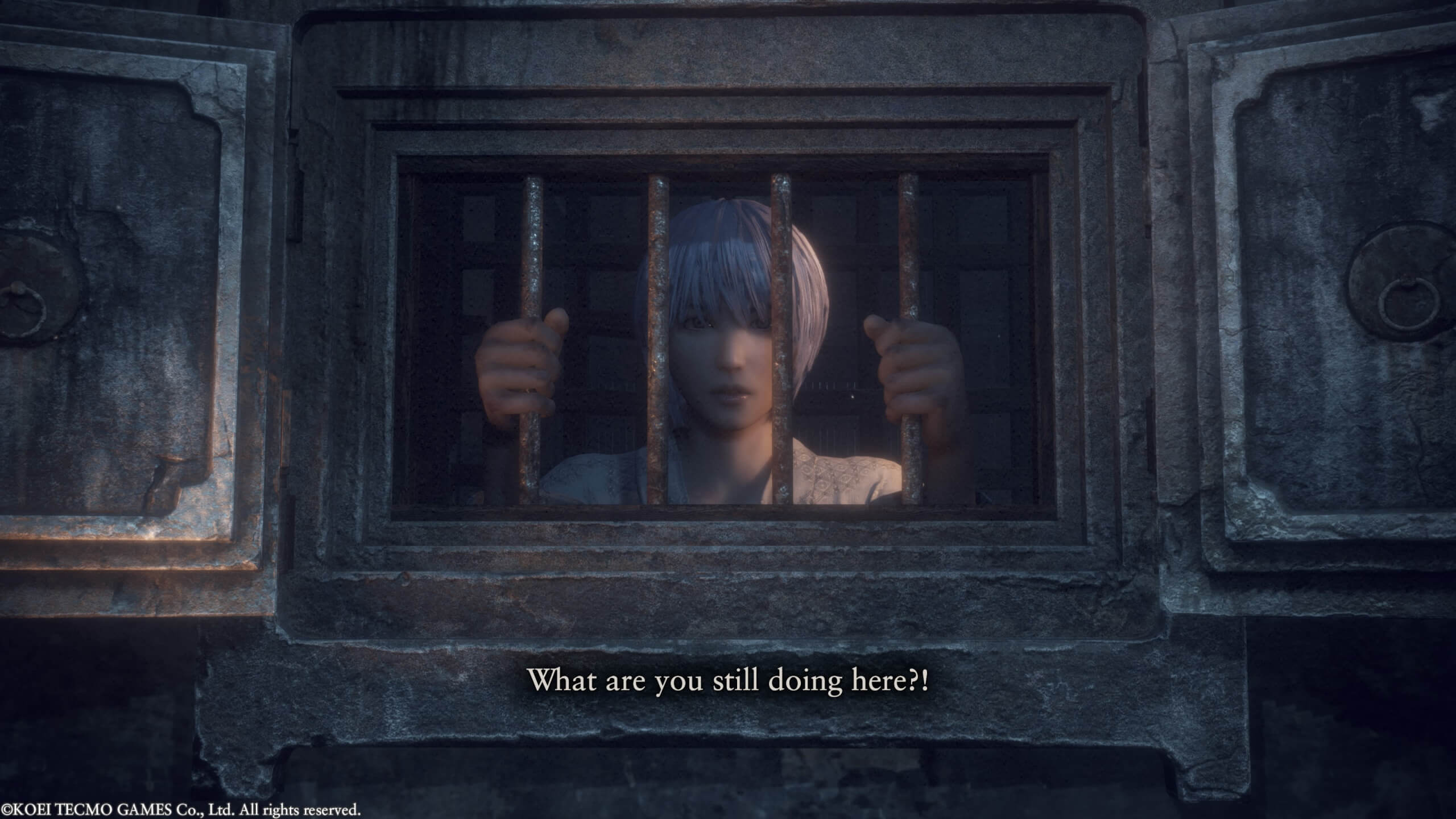 A young boy with white hair is holding onto the bars of his cell. He's speaking to the player and says "What are you still doing here?!".