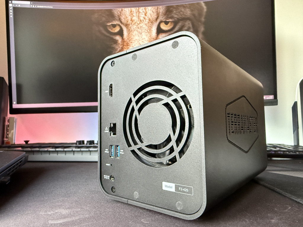 A black Terramaster F2-425 NAS device sits on a desk in front of a keyboard, with a monitor displaying a close-up of a wolf. Ports and vent fan are visible.