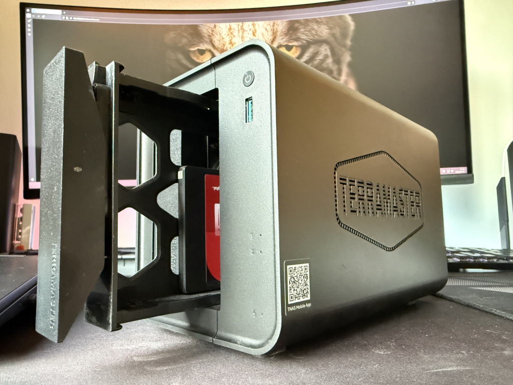 External hard drive enclosure labeled "TerraMaster" with an open front bay exposing a drive. A large monitor in the background shows a close-up of a cat's eyes.