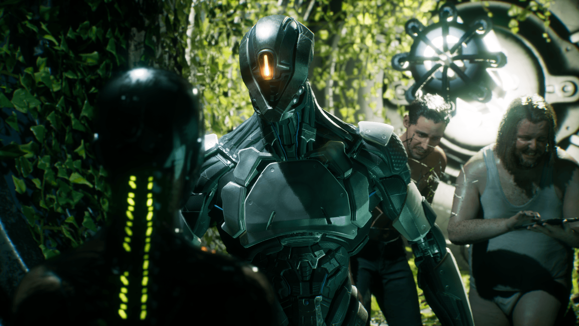 Four figures are in the shot, one shows the back of a robot with its spine glowing green. Infront of it is another robot, that looks larger and has one glowing optic which is orange. Two human men, are stood behind with the thinner man looking concerned while the larger is using a tablet, with a creepy face. 