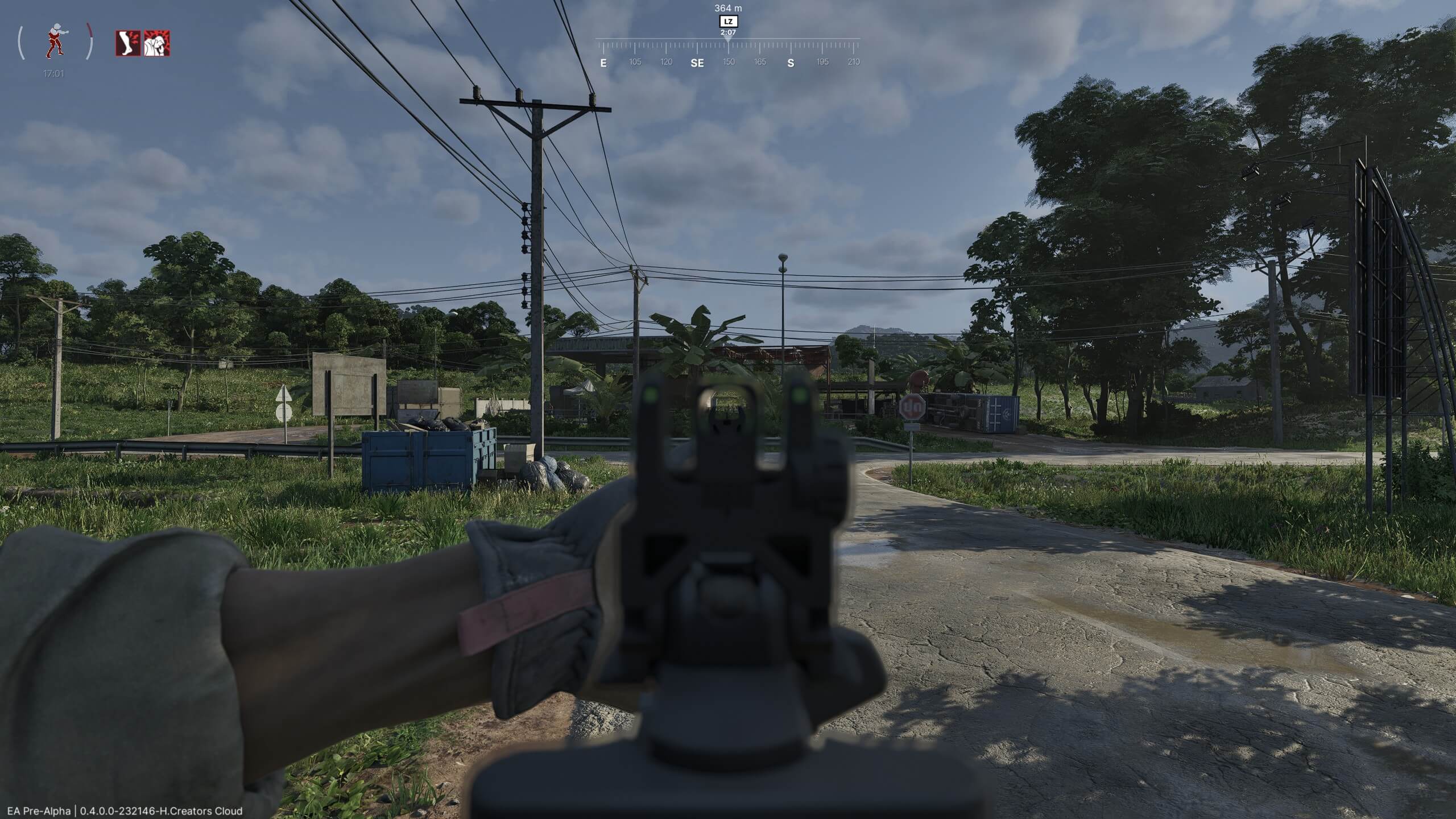 First-person shooter game view aiming down a gun at a rural roadside intersection with trees, power lines, and signs.