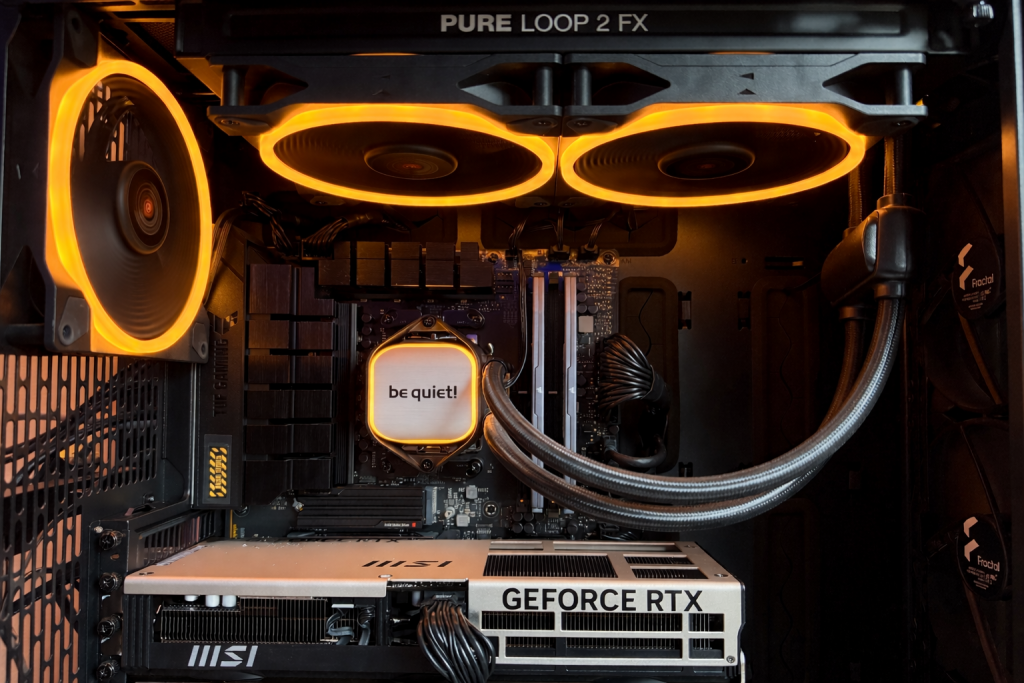 A computer build showcasing illuminated components, including three orange-ringed cooling fans, a “be quiet!” CPU cooler, and a GeForce RTX graphics card. The setup exudes a high-tech, gamer aesthetic.