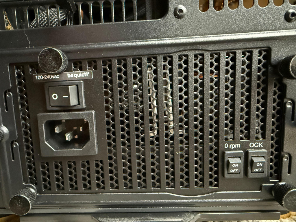 Close-up of a be quiet! dark power 14 computer power supply unit's back panel, featuring a honeycomb grill, power switch, AC input, and fan control switches labeled "0 rpm" and "OCK".