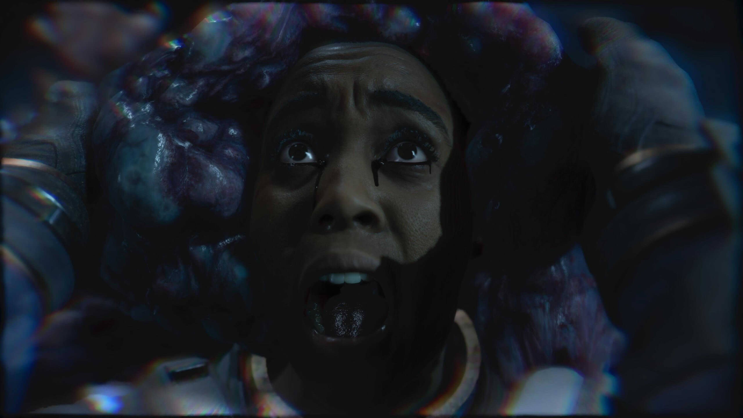 Close-up of a face, bleeding from the eyes being held by a dark, textured organic object with a sci-fi or alien appearance in low light.