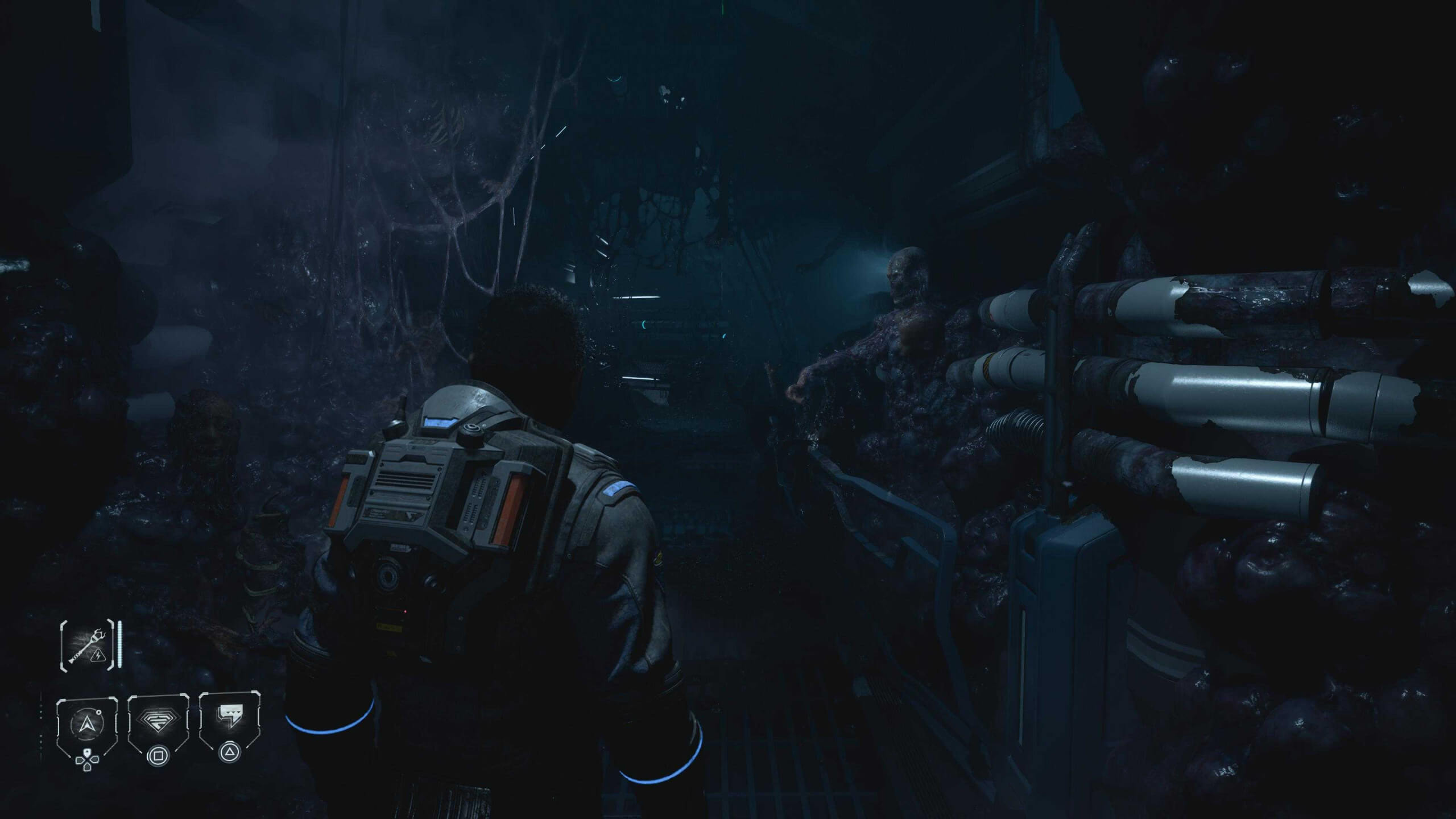 Game scene showing a character in a suit exploring a dark, eerie corridor with organic, mutated growths and pipes lining the walls.
