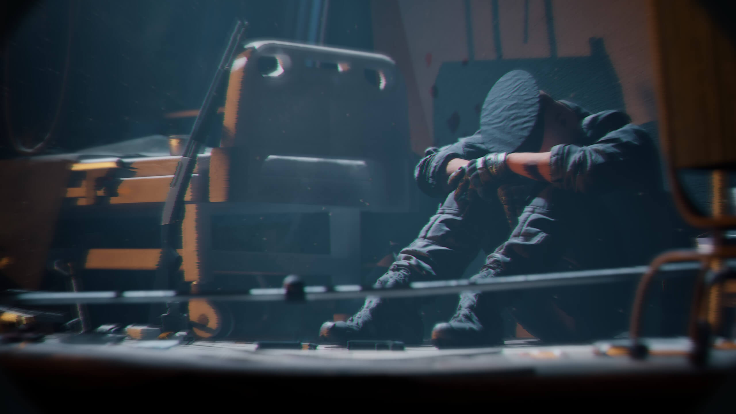 A man sat on the floor with his head in his arms with his knees up. He is wearing a police officers cap, and gloves. The area is illuminated around him showing a nearby shotgun.