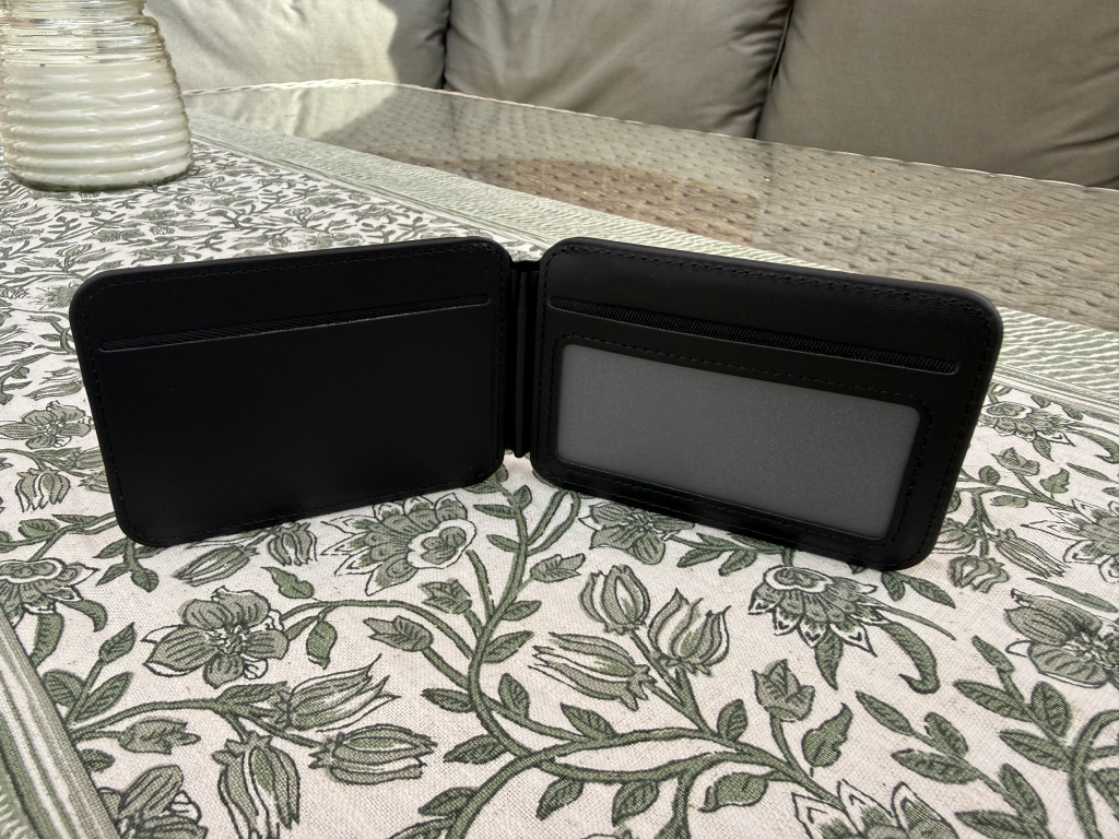 Open black wallet on a patterned tablecloth, with empty card slots and a clear ID window, situated on a glass-top table with a cosy background.