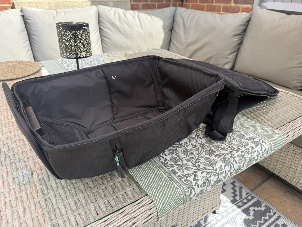 Open black laptop bag on a patterned outdoor table, surrounded by cushioned grey seating. The scene conveys a relaxed, casual atmosphere.