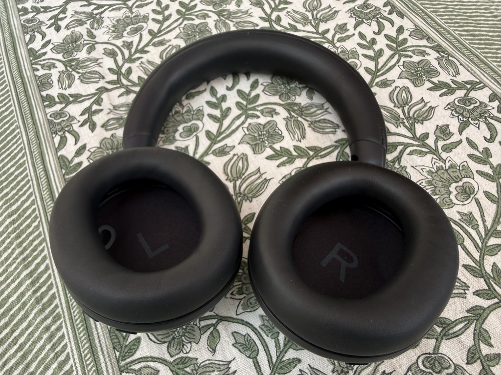 Black over-ear headphones with "L" and "R" markings placed on a patterned fabric surface with a green and white floral design.