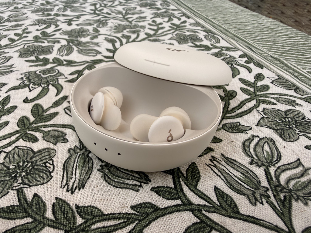 Open white charging case on a patterned tablecloth containing white earbuds. The scene conveys a sense of neatness and modern technology.