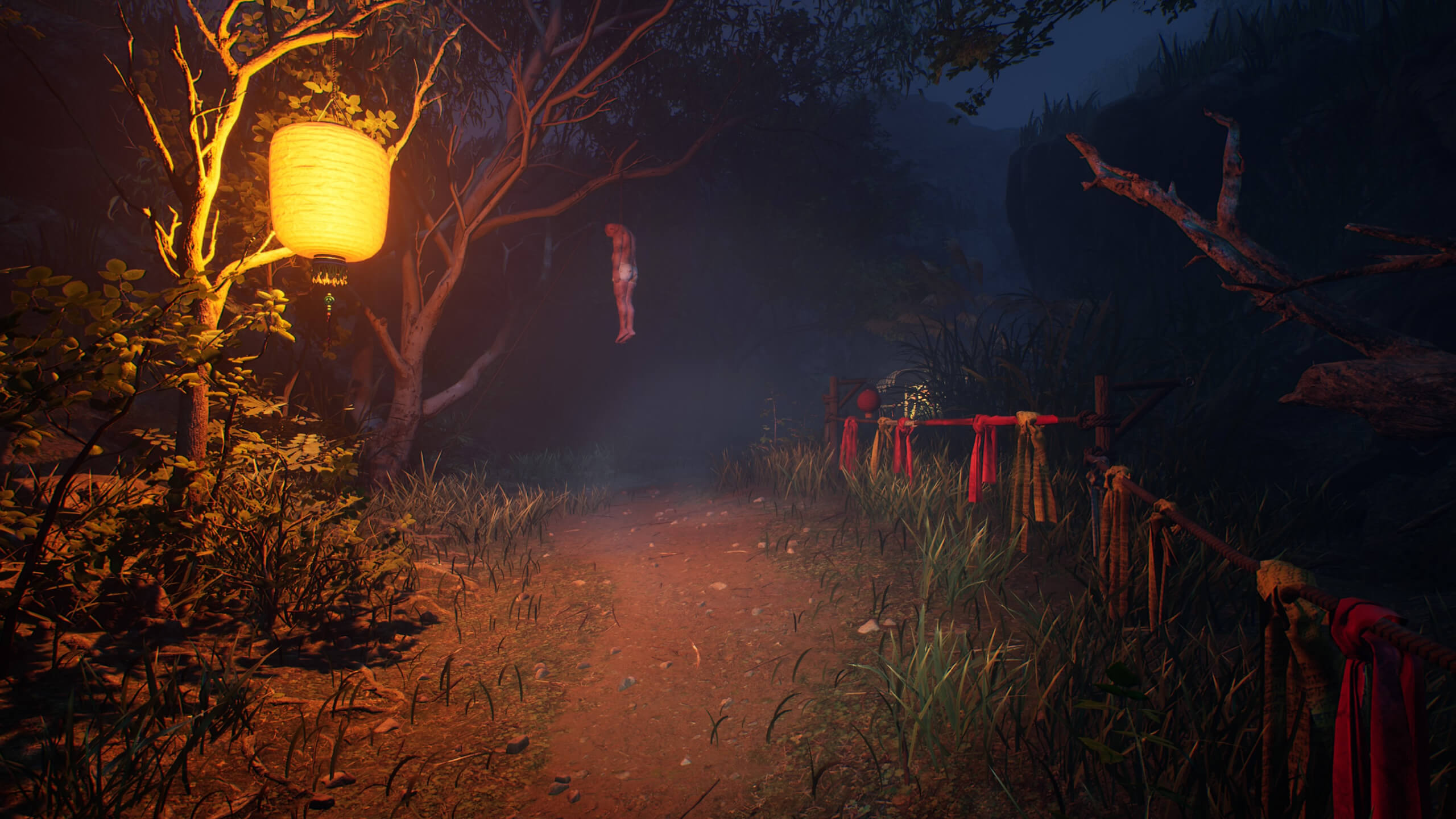 A path illuminated by a nearby paper lantern glowing in a tree. On the right side is a makeshift fence with white and red straps tied around it. In the distance is a person, who is hanging from a tree branch.