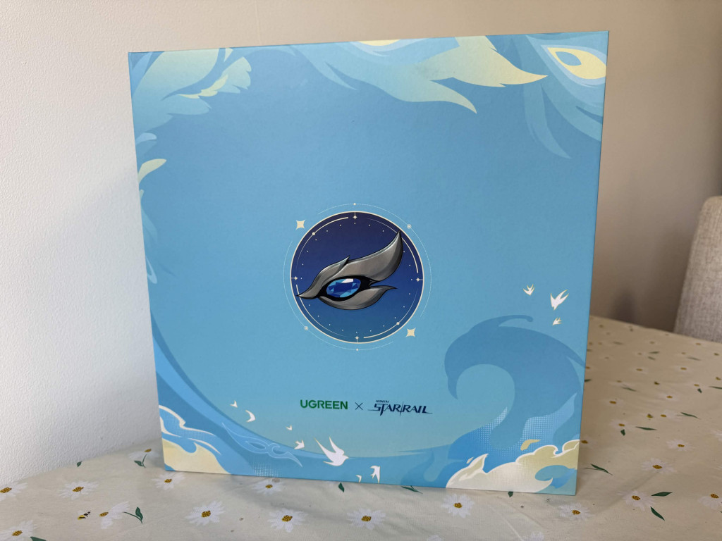 Photograph of a closed UGREEN Honkai: Star Rail Collector's box. The box is blue with peackock feathers and cosmic swirls all over it.