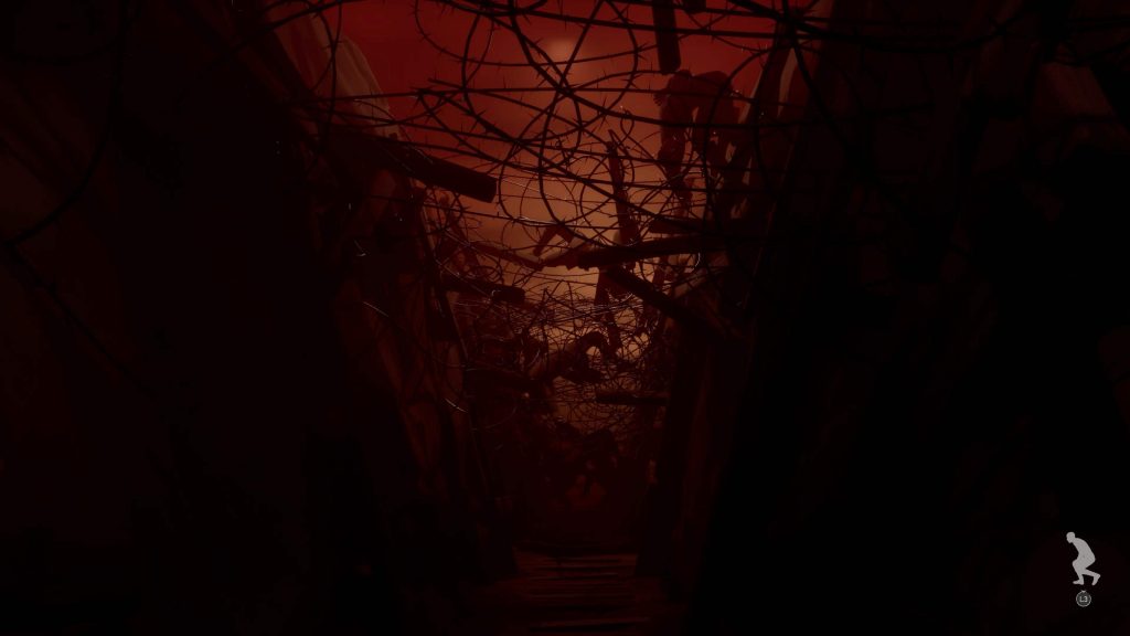 Dark, narrow corridor filled with twisted barbed wire and debris with bodies tangled within, illuminated by a red-orange light in the background.
