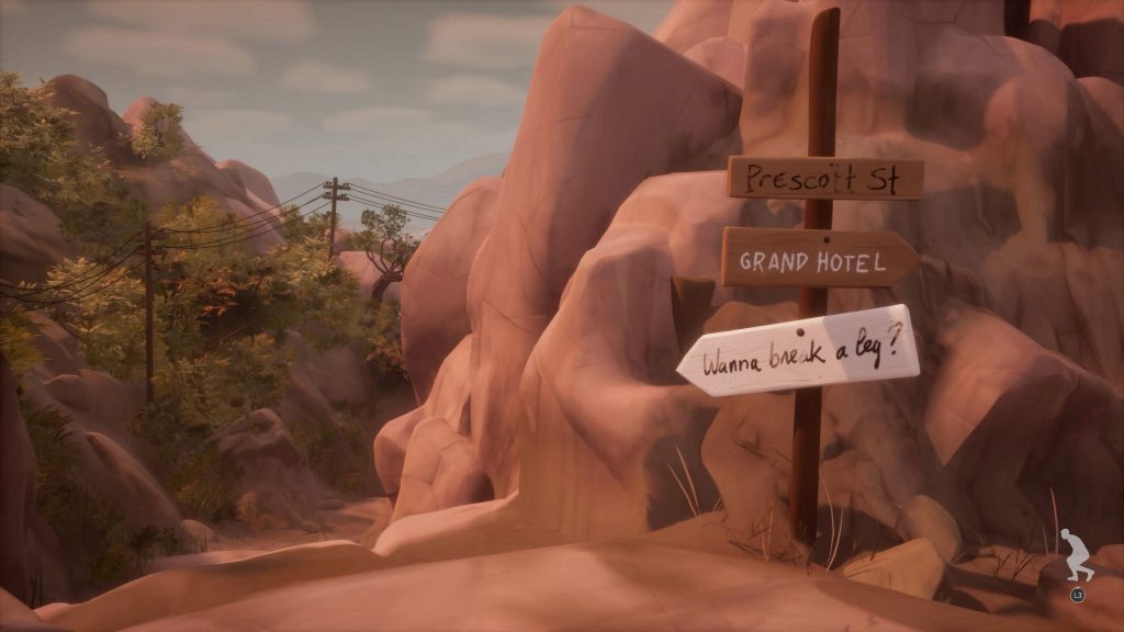 Signpost with handwritten arrows reading "Prescott St," "Grand Hotel," and "Wanna break a leg?" amid rocky terrain and trees under a cloudy sky.