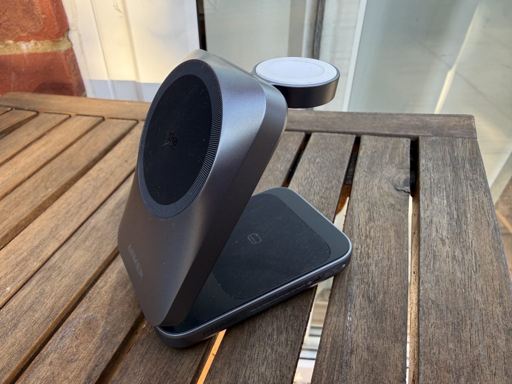 Anker's silver wireless charging pad atop a wooden table, with a small round charging puck behind it in warm sunlight.