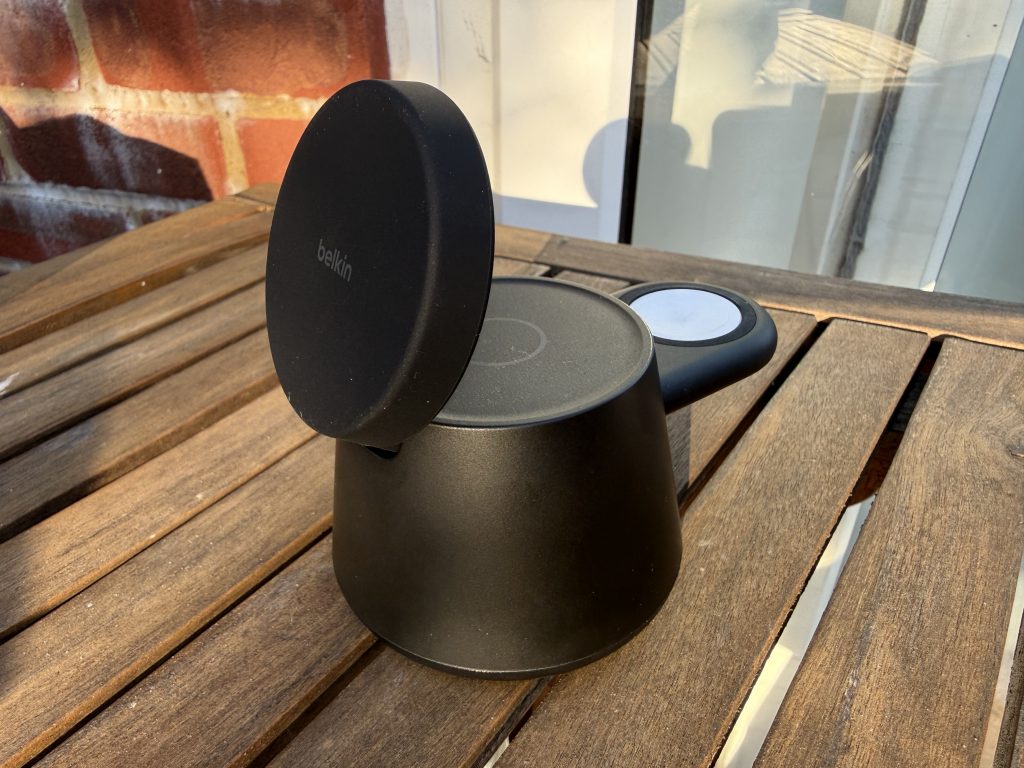 Black Belkin cylindrical electronic charging device with a raised round cover sits on a sunlit wooden table, creating a sleek, modern outdoor scene.