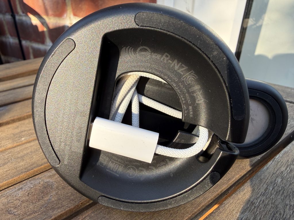 Close-up of the bottom of the Belkin black charging device with a white braided cord threaded through its centre, resting on a sunlit wooden table.