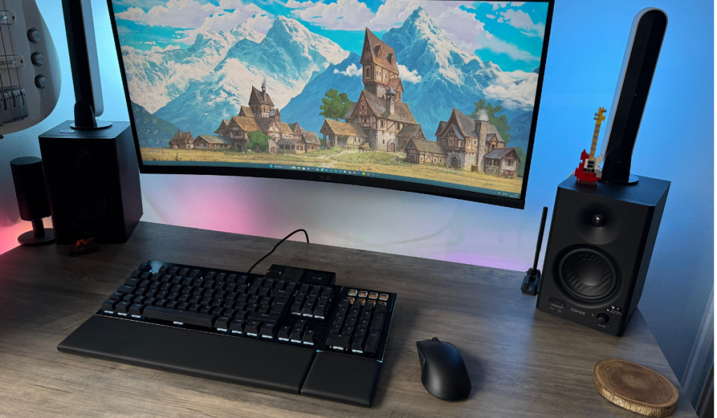 be quiet dark mount keyboard and dark ergo mouse sit on a wooden desk. On the wall a monitor shows a village scene.