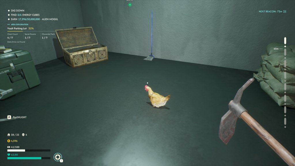 First-person view in a game showing a chicken on a dark floor, with a pickaxe, treasure chest, broom, and sandbags in a gray room.