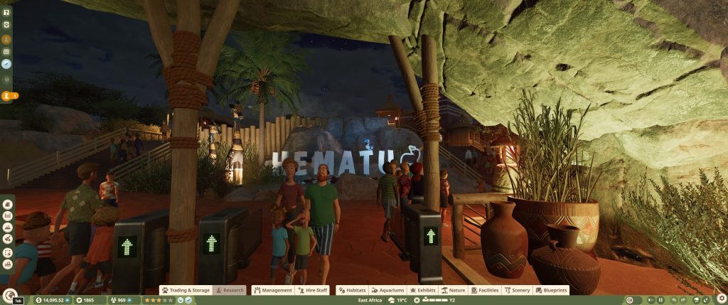 A night-time scene shows people exploring a warmly lit entance, with palm trees, stone paths, clay pots, and large rock formations creating an adventurous atmosphere.